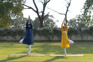 A couple performing yoga in traditional Indian attire in a serene outdoor park setting.